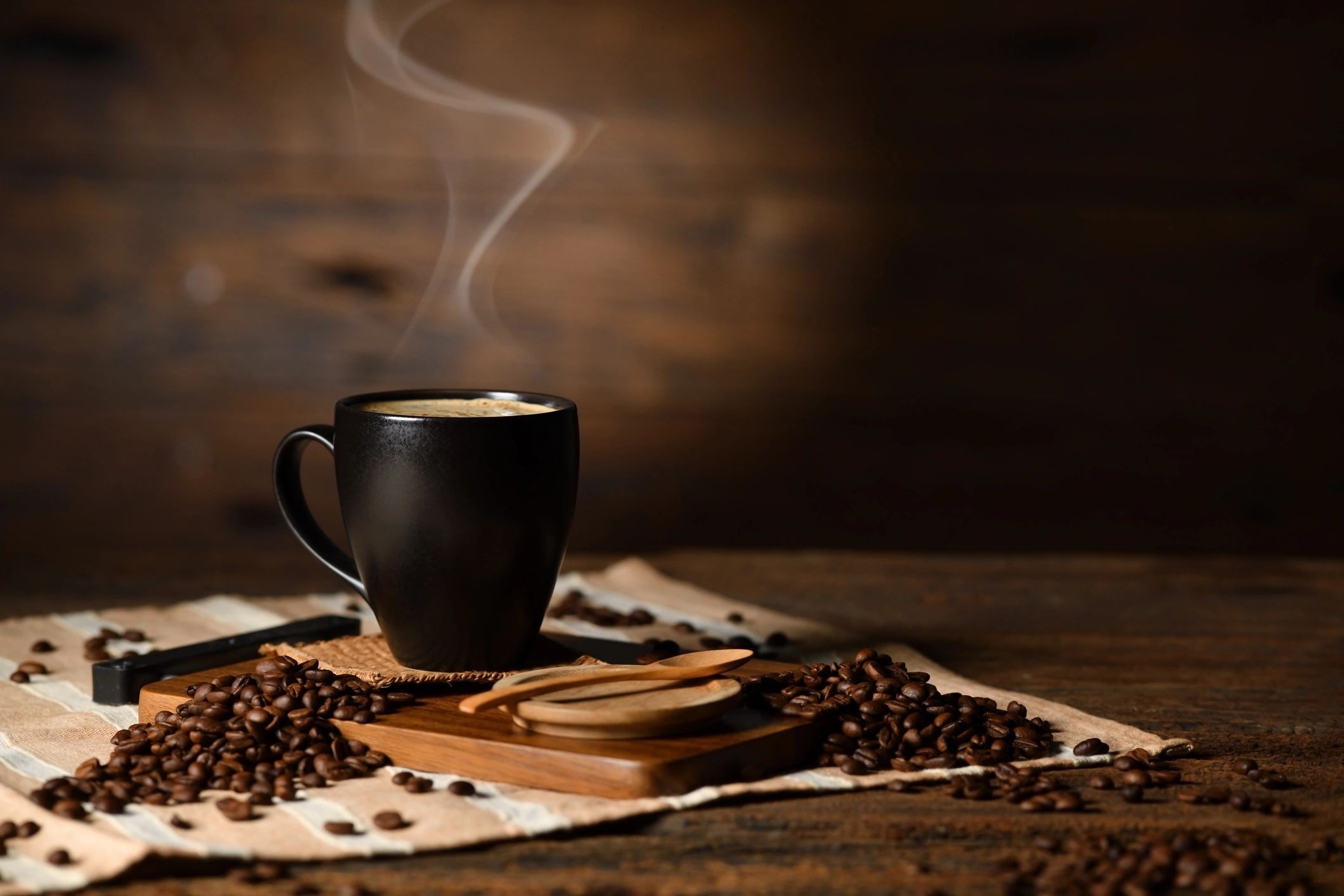 Steaming cup of coffee with beans on a wooden table