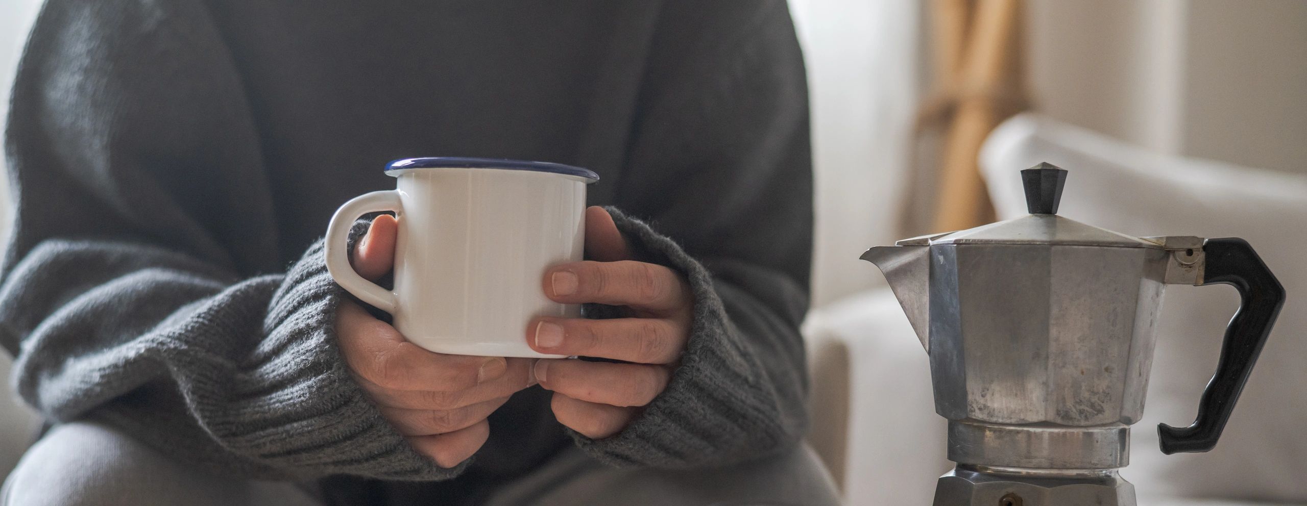 Person holding a coffee mug beside a moka pot